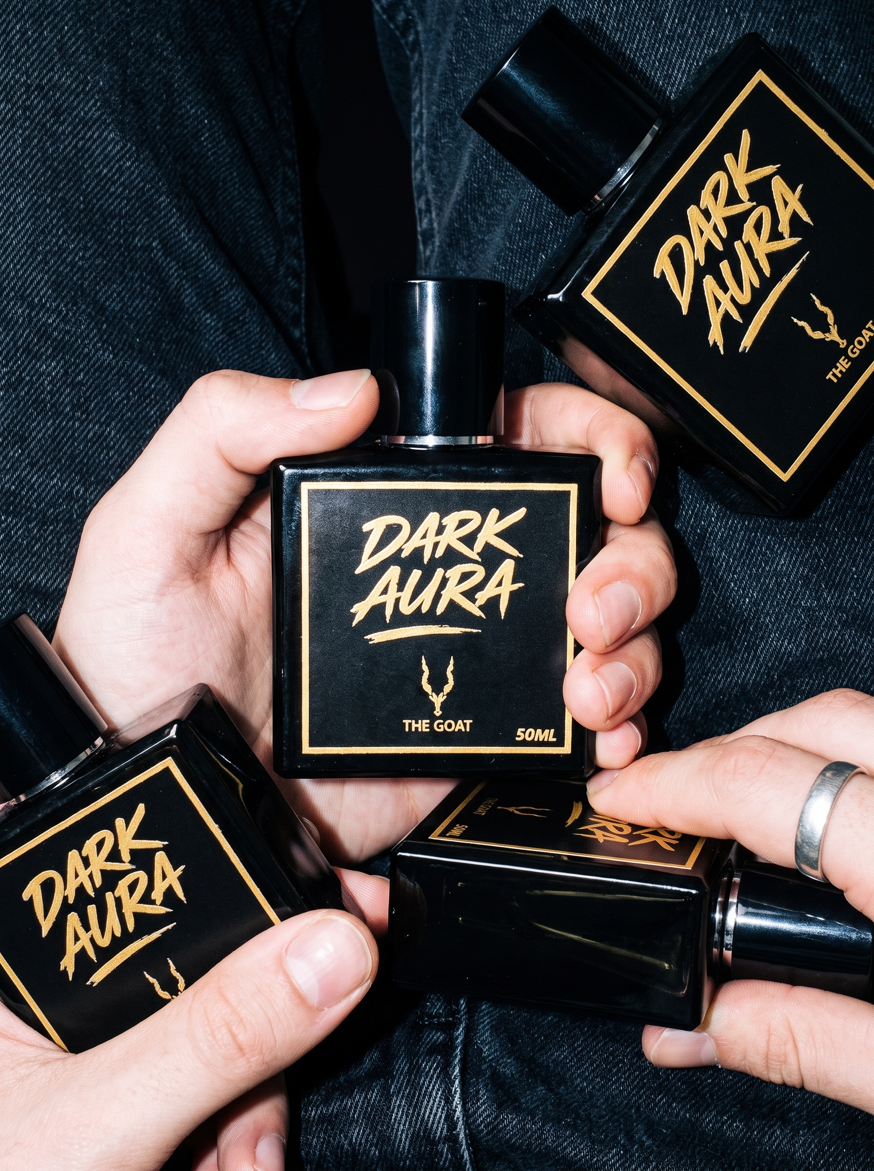Hands holding Dark Aura perfume bottles by The Goat Fragrance against denim